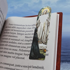 May include: A bookmark featuring a stained glass image of a woman in a white robe with a halo, kneeling before a figure in a black robe. The bookmark is on a book with text about a woman in a white robe with a halo, kneeling before a figure in a black robe.