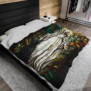 Puede incluir: Una colcha con un diseño de vidriera que representa una figura religiosa con los brazos extendidos, rodeada por una escena de bosque. El diseño incluye tonos de blanco, amarillo, verde y marrón, creando una estética detallada y artística.