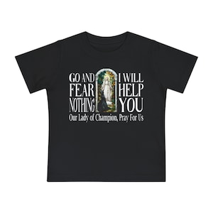 May include: A black short-sleeved t-shirt featuring a central graphic of a figure in a white robe within an arched frame. The text reads: GO AND FEAR NOTHING I WILL HELP YOU Our Lady of Champion, Pray For Us in white capital letters.