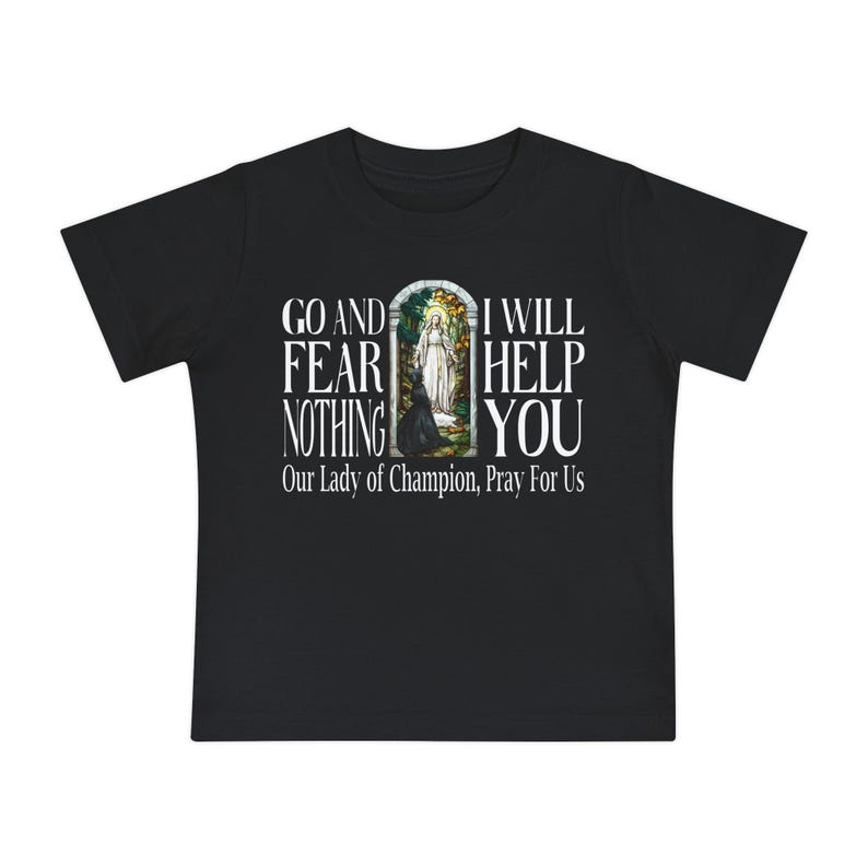 May include: A black short-sleeved t-shirt featuring a central graphic of a figure in a white robe within an arched frame. The text reads: GO AND FEAR NOTHING I WILL HELP YOU Our Lady of Champion, Pray For Us in white capital letters.