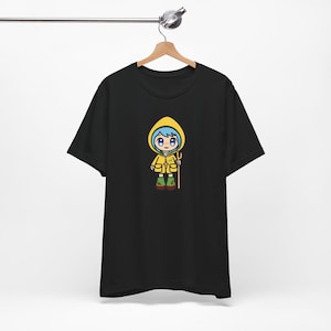 Könnte beinhalten: Schwarzes T-Shirt mit einer Cartoon-Illustration eines Mädchens, das einen gelben Regenmantel trägt und einen Stock hält. Das Mädchen hat blaue Haare und trägt grüne Stiefel.
