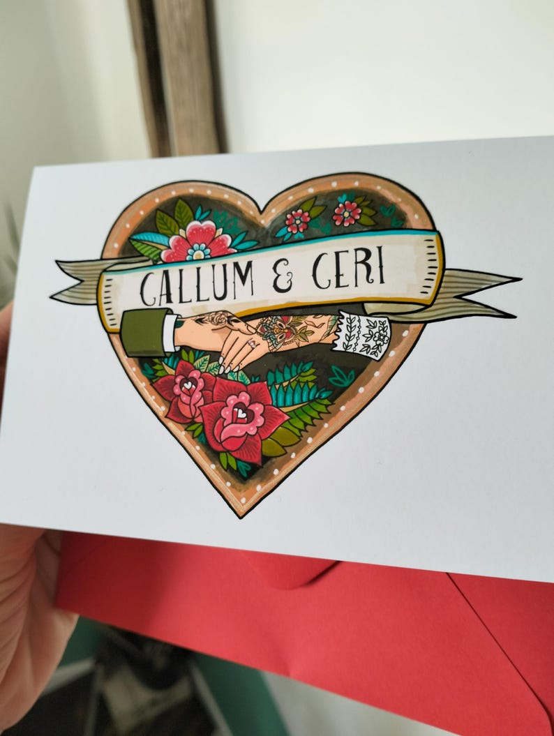 May include: A white greeting card featuring a heart-shaped illustration with red roses, green leaves, and a banner reading CALLUM & CERI. The design depicts two hands holding each other, one with a green sleeve and one with a white lace cuff.