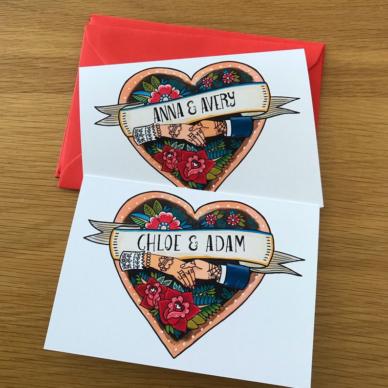 Two white cards with a red envelope. Each card has a heart-shaped design with a couple's names and a banner. The first card has the names 'Anna & Avery' and the second card has the names 'Chloe & Adam'.