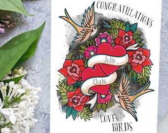 May include: A white greeting card with a tattoo-style design. Two red hearts with the names "Julie" and "Chris" on banners are surrounded by red roses, pink flowers, and green leaves. Two tan birds and the words "CONGRATULATIONS" and "LOVE BIRDS" are also featured.