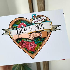 May include: A rectangular greeting card featuring a heart-shaped illustration with a Las Vegas sign at the top. A banner across the center reads RACH & PAUL. The design includes two hands holding each other, surrounded by red and pink flowers and green leaves.