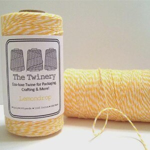 May include: Two spools of yellow and white twisted cotton twine. The upright spool features a white label with the text The Twinery, Eco-luxe Twine for Packaging, Crafting & More!, Lemondrop, 4 ply, 240 yards, 100% Cotton, USA Made.