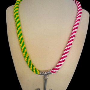 May include: A beaded necklace with a silver-colored axe pendant. The necklace is made of yellow and green beads on one side and red and white beads on the other. The pendant is a double-bladed axe.