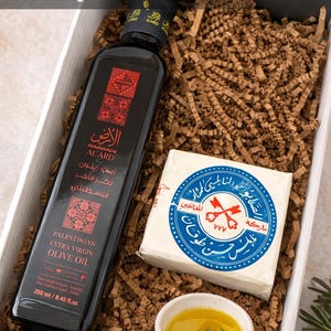 May include: Palestinian olive oil and soap gift box. The box contains a dark bottle of Al'Ard Extra Virgin Olive Oil, a bar of Nablus Olive Oil Soap, and a small dish of olive oil. The box is filled with brown paper filler.