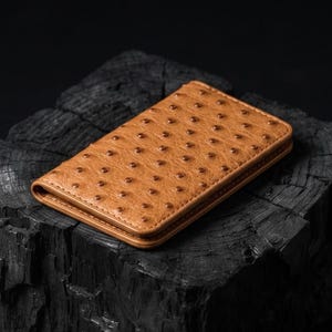 May include: A rectangular tan wallet featuring a distinct textured surface with evenly spaced, dark circular indentations across the exterior. The wallet has clean, stitched edges and a slim, folded profile, showcasing a consistent pattern throughout.