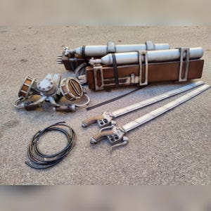 Puede incluir: Un conjunto de accesorios de la serie de anime, Ataque a los Titanes. El conjunto incluye dos espadas, un paquete de bombonas de gas, una máscara y una manguera enrollada. Las espadas tienen empuñaduras y hojas detalladas. El paquete de bombonas de gas es marrón con cilindros plateados.
