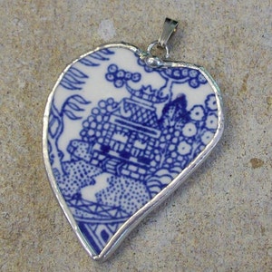 May include: A blue and white porcelain pendant shaped like a heart, with a silver border. The pendant features a traditional Chinese design with a pagoda and flowers.