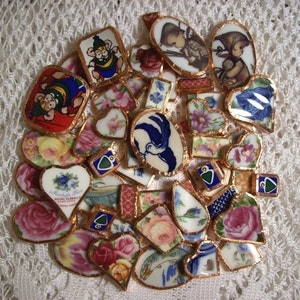 May include: A collection of vintage porcelain tiles with gold trim, featuring floral patterns, birds, and children. The tiles are arranged in a circular pattern and have a variety of colours, including blue, pink, green, and white.