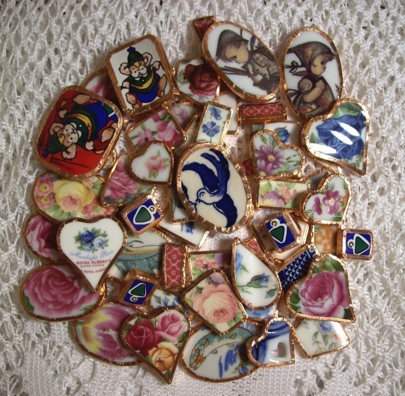 May include: A collection of vintage porcelain tiles with gold trim, featuring floral patterns, birds, and children. The tiles are arranged in a circular pattern and have a variety of colours, including blue, pink, green, and white.