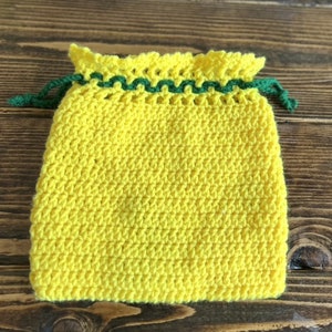 May include: A handmade yellow knitted drawstring bag with a green trim and drawstring. The bag is made of a textured yarn and has a ruffled top. The drawstring is a dark green color.