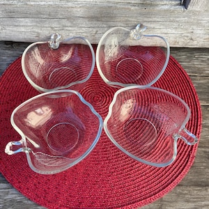 May include: Set of four clear glass apple-shaped bowls. The bowls are on a red woven placemat.