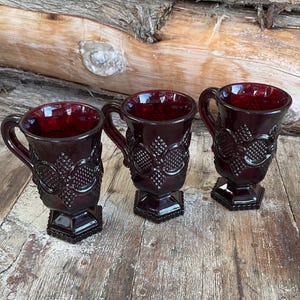 Peut inclure: Trois tasses en verre rouge avec un motif texturé et un pied. Les tasses sont de couleur rouge foncé et sont en verre.