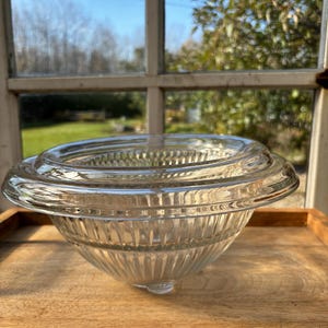 以下が含まれることがあります： フルーテッドデザインの透明なガラスボウル。ボウルは幅広のリムと丸みを帯びたベースを持っています。木製の表面の上に置かれています。