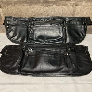 Puede incluir: Dos cinturones de herramientas de cuero negro con múltiples bolsillos y detalles metálicos. Los cinturones están hechos de cuero grueso y duradero y tienen un diseño clásico.