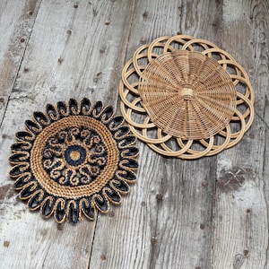 Può includere: Due sottopiatti decorativi intrecciati. Uno è di colore beige naturale con un design circolare e l'altro è una combinazione di beige e nero con un motivo floreale. I sottopiatti sono su una superficie di legno invecchiato.