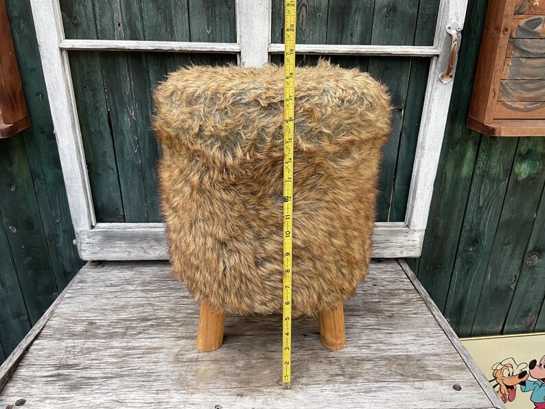 Pu&ograve; includere: Uno sgabello in finta pelliccia marrone e nera con gambe in legno. Lo sgabello &egrave; alto 43 cm.