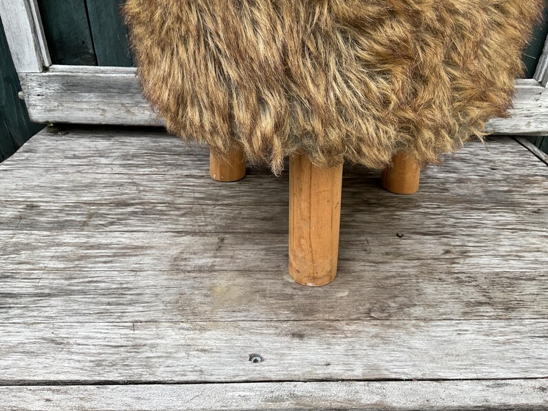 Pu&ograve; includere: Uno sgabello in pelliccia sintetica marrone e nero con quattro gambe in legno.