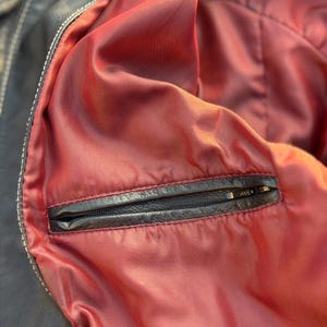 May include: Close-up of the inside of a black leather jacket, showing a red lining and a zippered pocket.