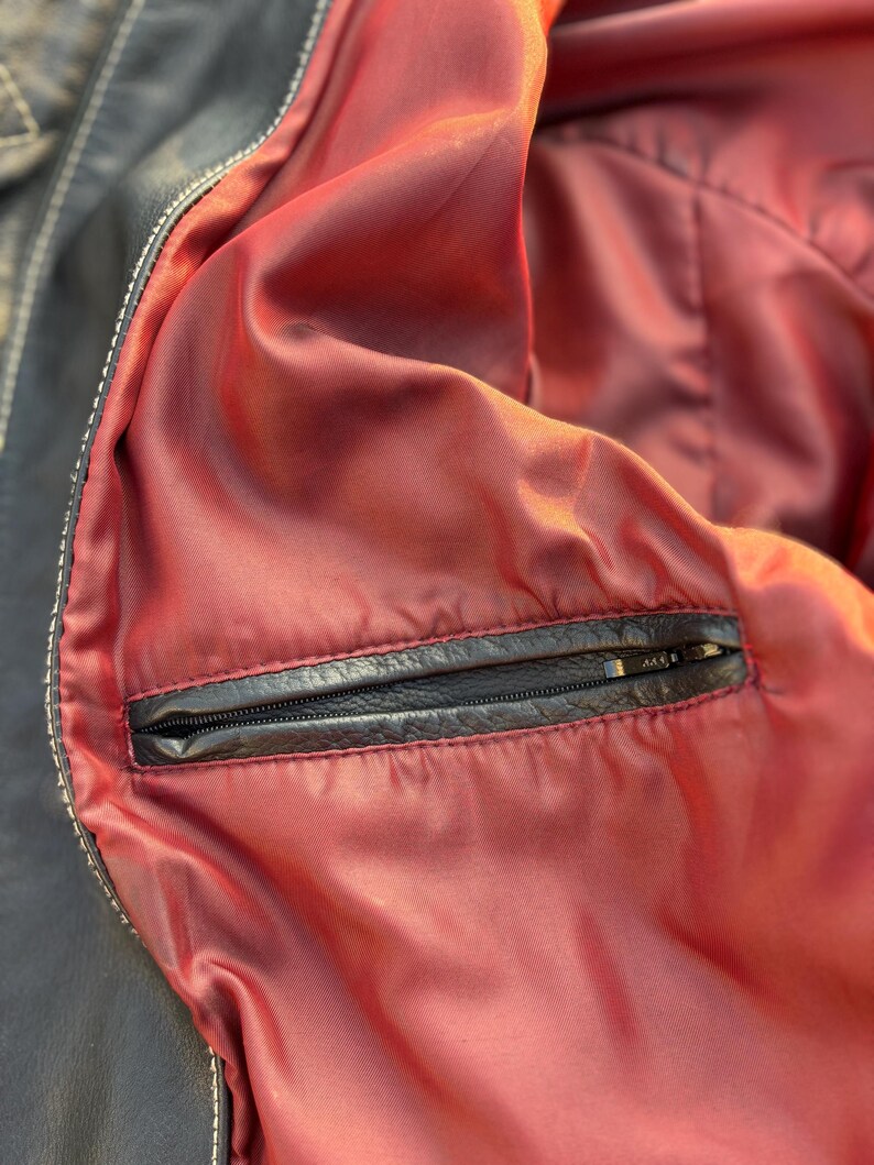 May include: Close-up of the inside of a black leather jacket, showing a red lining and a zippered pocket.
