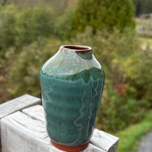 Könnte beinhalten: Eine kleine, grüne Keramikvase mit braunem Rand. Die Vase hat eine glatte, glänzende Oberfläche und eine leicht abgerundete Form.