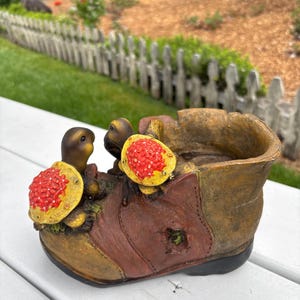 May include: A decorative planter shaped like a worn boot, featuring two turtle figurines with red and yellow accents. The boot is brown and tan with a black sole, designed for outdoor use.