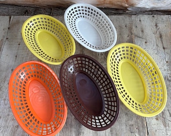 May include: An assortment of five oval-shaped plastic baskets in various colors: yellow, white, orange, brown, and yellow. The baskets have a lattice design and are empty.