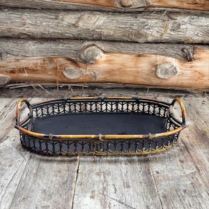 May include: An oval black metal tray with gold accents. The tray has a decorative openwork design around the edges and two curved handles. The tray is sitting on a wooden surface.