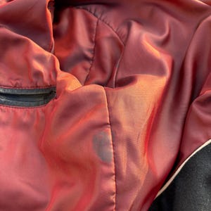 May include: The inside of a black leather jacket with a red satin lining. The lining has a small dark stain.