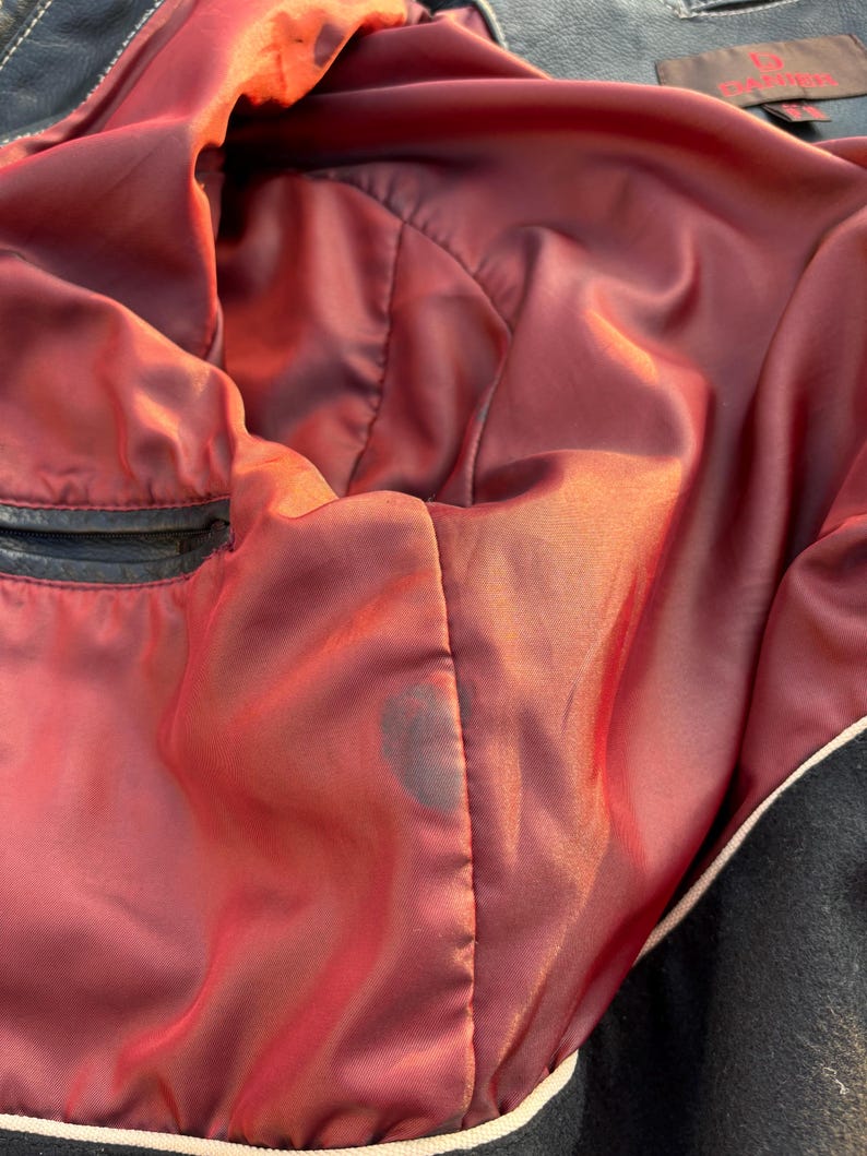 May include: The inside of a black leather jacket with a red satin lining. The lining has a small dark stain.