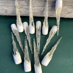 May include: Ten white plastic icicle Christmas tree ornaments. The icicles are clear and have a textured surface. The ornaments have a white base.