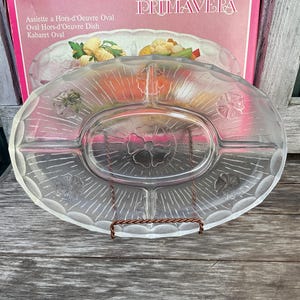 Könnte beinhalten: Eine klare Glasservierplatte mit floralem Design. Die Platte ist in fünf Abschnitte unterteilt und hat einen erhöhten Rand.