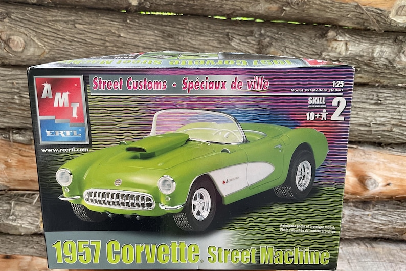 May include: A model kit box for a 1957 Corvette Street Machine. The box is green, white and black with a picture of the car on the front. The text on the box reads "1957 Corvette Street Machine" and "Street Customs Sp&eacute;ciaux de ville".