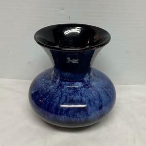 Puede incluir: Un jarrón de cerámica azul y negro con un esmalte blanco. El jarrón tiene una base ancha y un cuello estrecho.