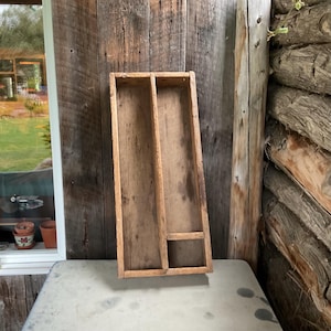 Puede incluir: Una bandeja de madera rústica con tres compartimentos. La bandeja está hecha de madera natural con un acabado desgastado. Tiene una forma rectangular y es perfecta para organizar objetos pequeños.