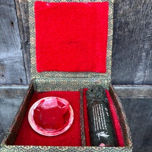 May include: An open, ornate box with a red velvet interior. Inside, a red ink pad and a dark green, carved stone seal are visible. The box has a decorative, patterned exterior and a wooden clasp.