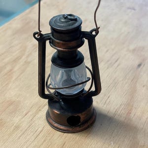 May include: A vintage-style metal pencil sharpener shaped like a lantern. The sharpener is black and copper with a clear plastic window. It has a handle on top and a pencil sharpening hole on the bottom.