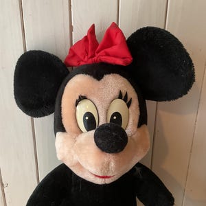 May include: A plush Minnie Mouse doll with black fur, large black ears, and a red bow. The doll has a pink face, large eyes, and a black nose. The doll is a classic Disney character.