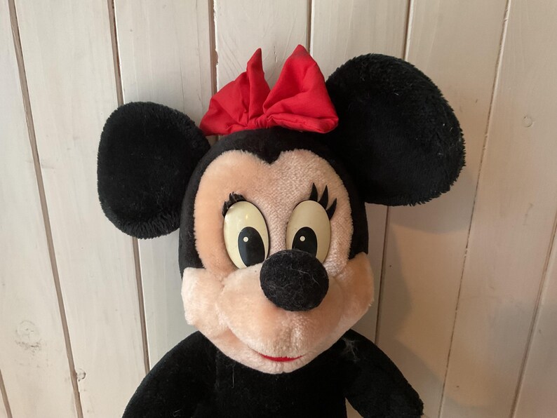May include: A plush Minnie Mouse doll with black fur, large black ears, and a red bow. The doll has a pink face, large eyes, and a black nose. The doll is a classic Disney character.