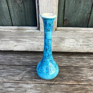May include: A small, blue ceramic vase with a speckled glaze. The vase has a narrow neck and a rounded base.