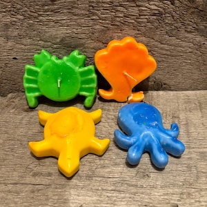 Könnte beinhalten: Vier bunte Kerzen in Form von Meeresbewohnern. Ein grüner Krebs, eine orangefarbene Muschel, eine gelbe Schildkröte und ein blauer Tintenfisch.