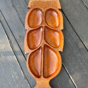 May include: A wooden serving tray shaped like a fish with five individual serving bowls. The tray is a light brown color with a darker brown wood grain.
