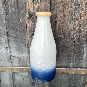 以下が含まれることがあります： 前面に「Lait」と印刷された、青色のグラデーションデザインの白いセラミック製ミルクボトル。ボトルには黄色の蓋が付いています。