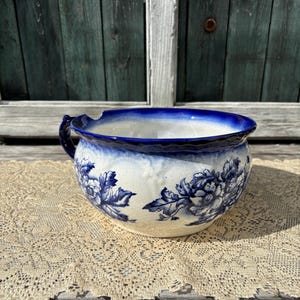 Puede incluir: Un macetero de cerámica azul y blanco con un diseño floral. El macetero tiene una forma ancha y redonda y una sola asa.