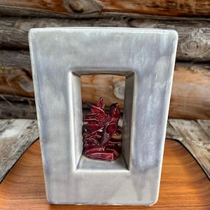 May include: A grey ceramic vase with a rectangular opening. Inside the opening is a red ceramic bird sculpture.