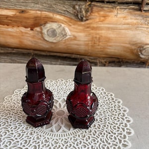 Peut inclure: Une paire de salières et poivrières en verre rouge foncé présentant un motif pressé à facettes avec une texture en grille en forme de losange sur le corps inférieur et une base hexagonale. Chaque récipient a un couvercle pointu amovible.