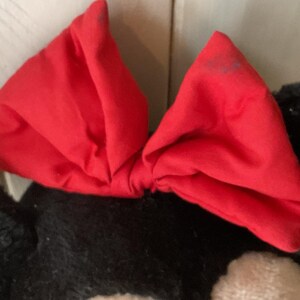 May include: A vivid red bow, possibly made of fabric, is the central element, set against a black and white background. The bow's bright colour provides a contrast to the darker tones, creating a visually striking image. The bow's shape suggests it could be part of a larger item.